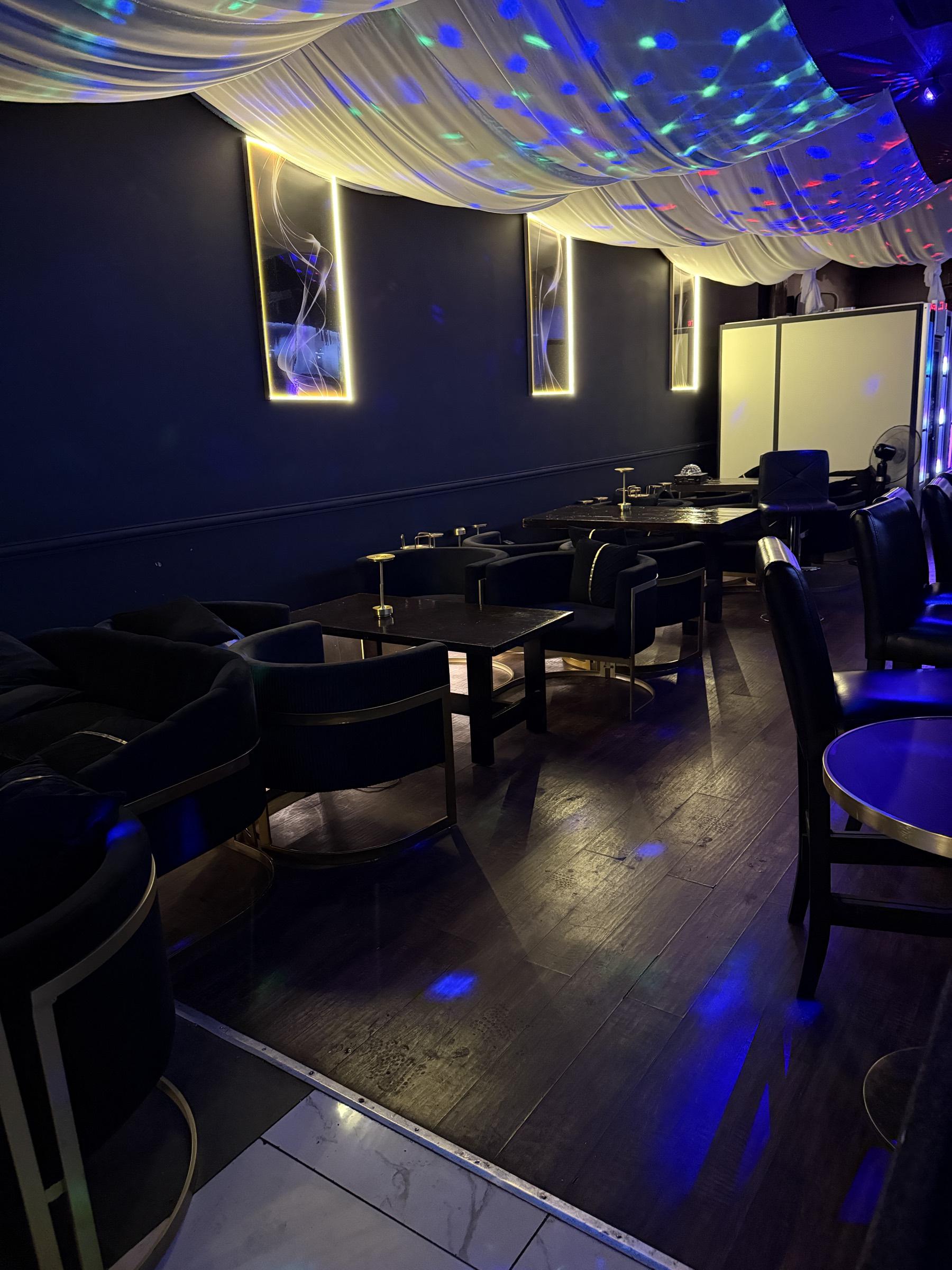 Curved navy armchairs with gold frames arranged around cocktail tables, where the dark wood floor meets a white marble dance floor.