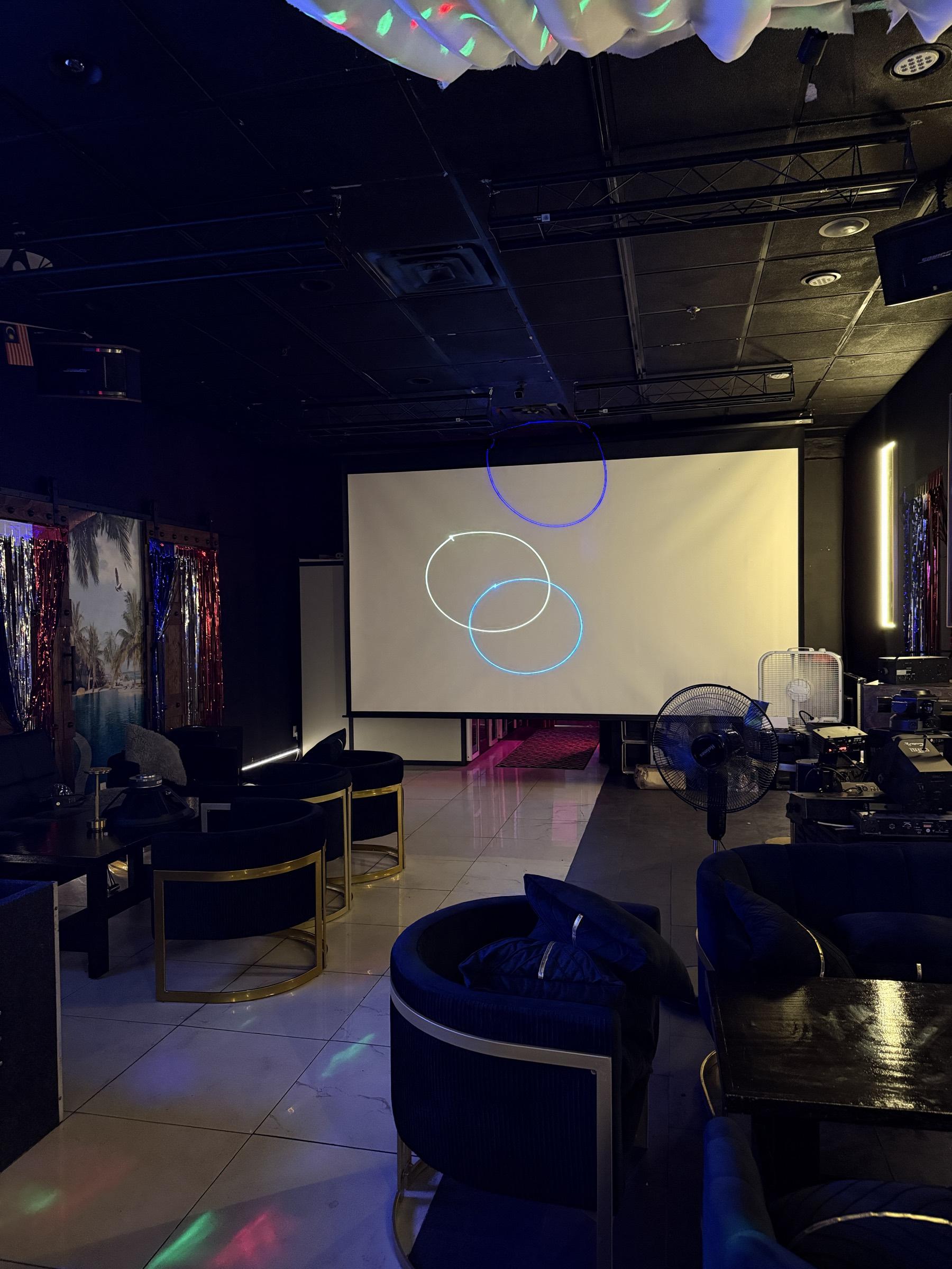 The projection screen and white marble floor, with a tinsel photo backdrop to one side and gold-framed velvet chairs in front.