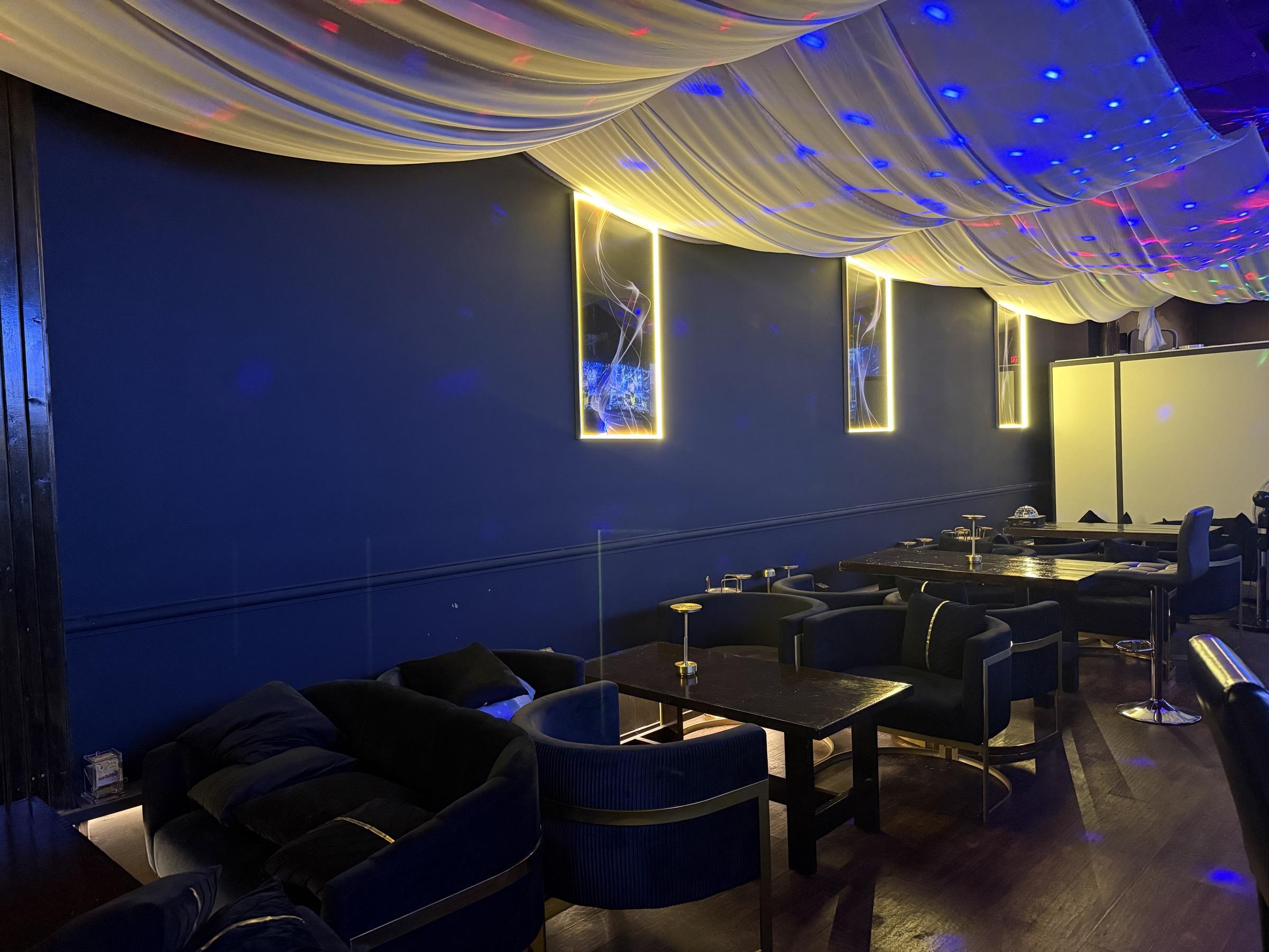 Rows of navy velvet armchairs and low black tables running the length of the lounge, lit by small brass table lamps.