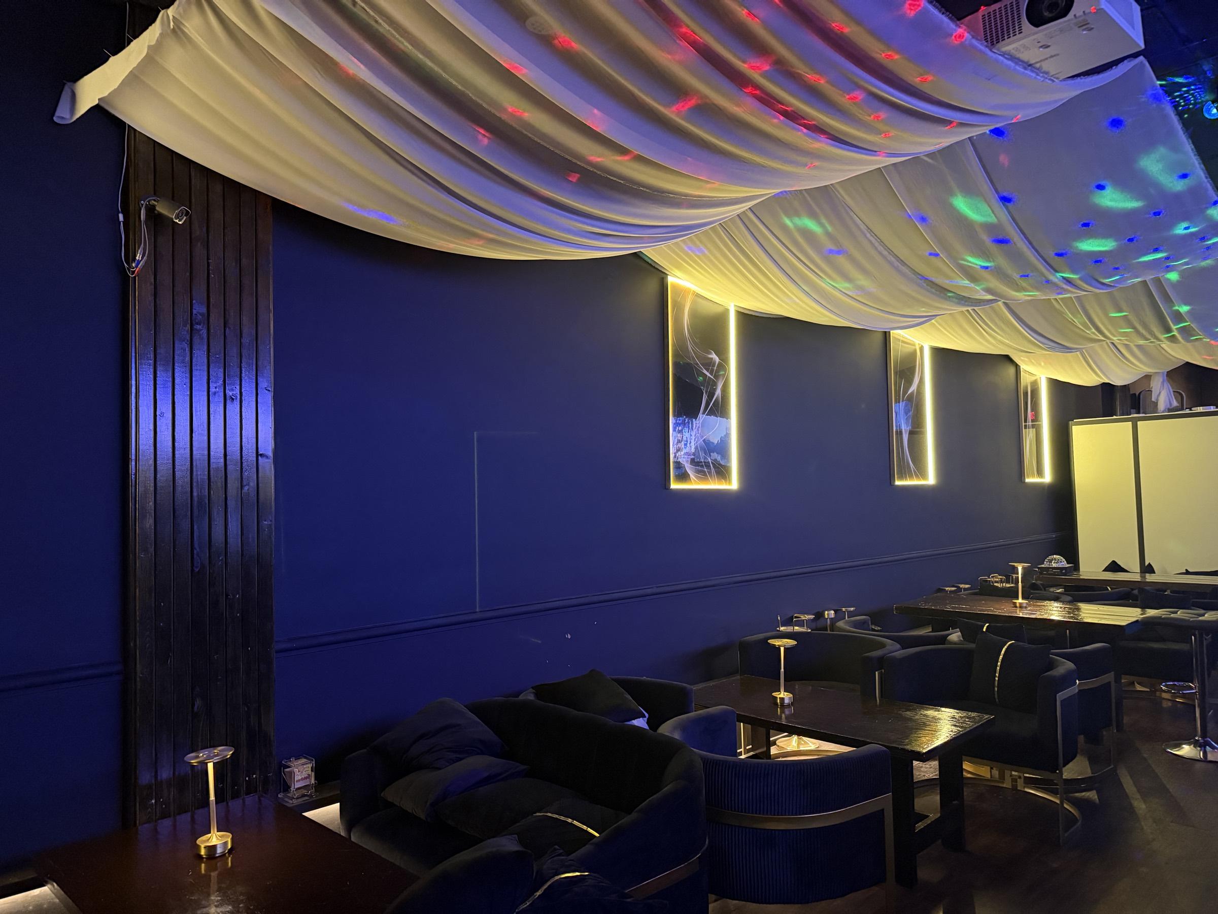 Navy wall with gold wainscoting and backlit artwork, with velvet loveseats and gold-framed armchairs in the foreground.
