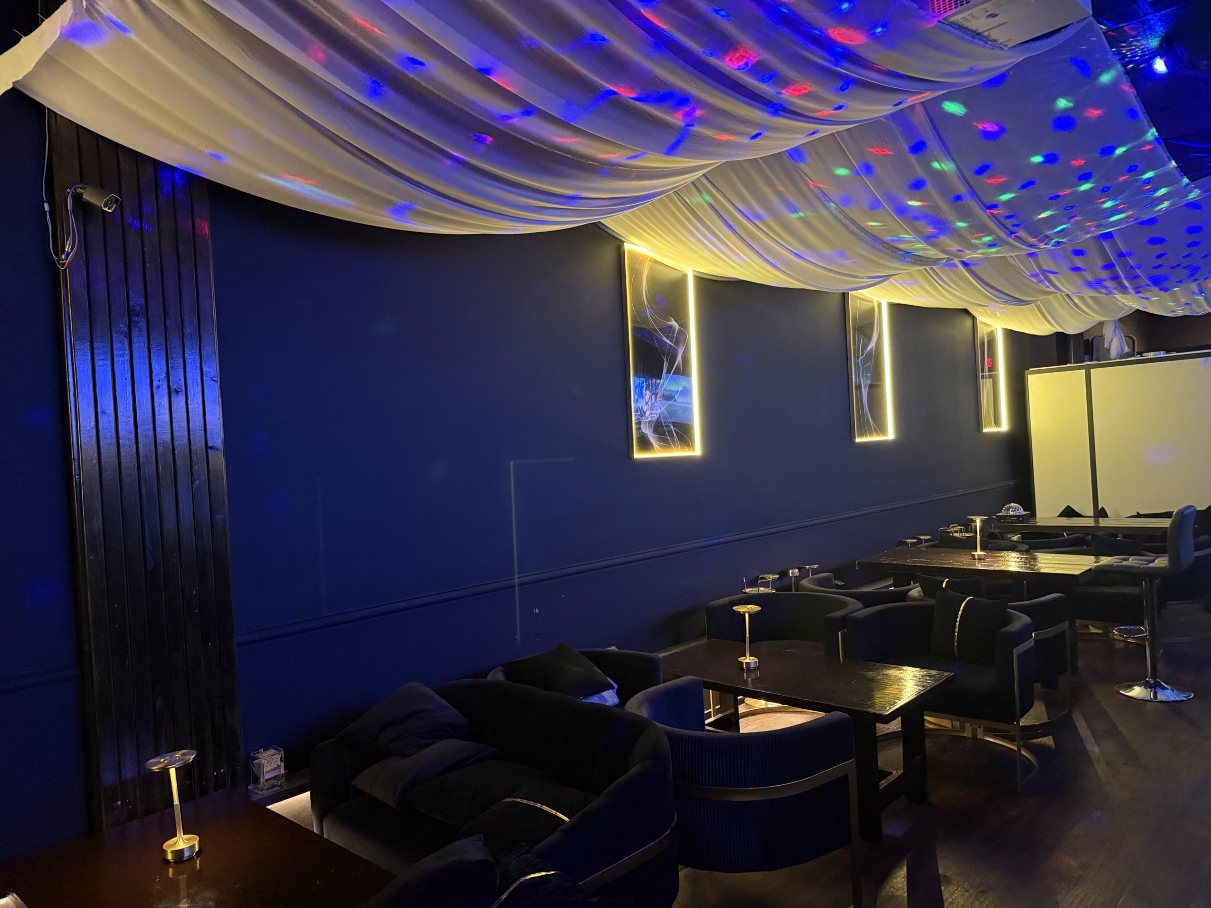 The full length of Bar Vier's lounge: deep navy walls with gold trim, backlit gold-framed artwork, and ivory fabric draped across the ceiling above navy velvet armchairs.